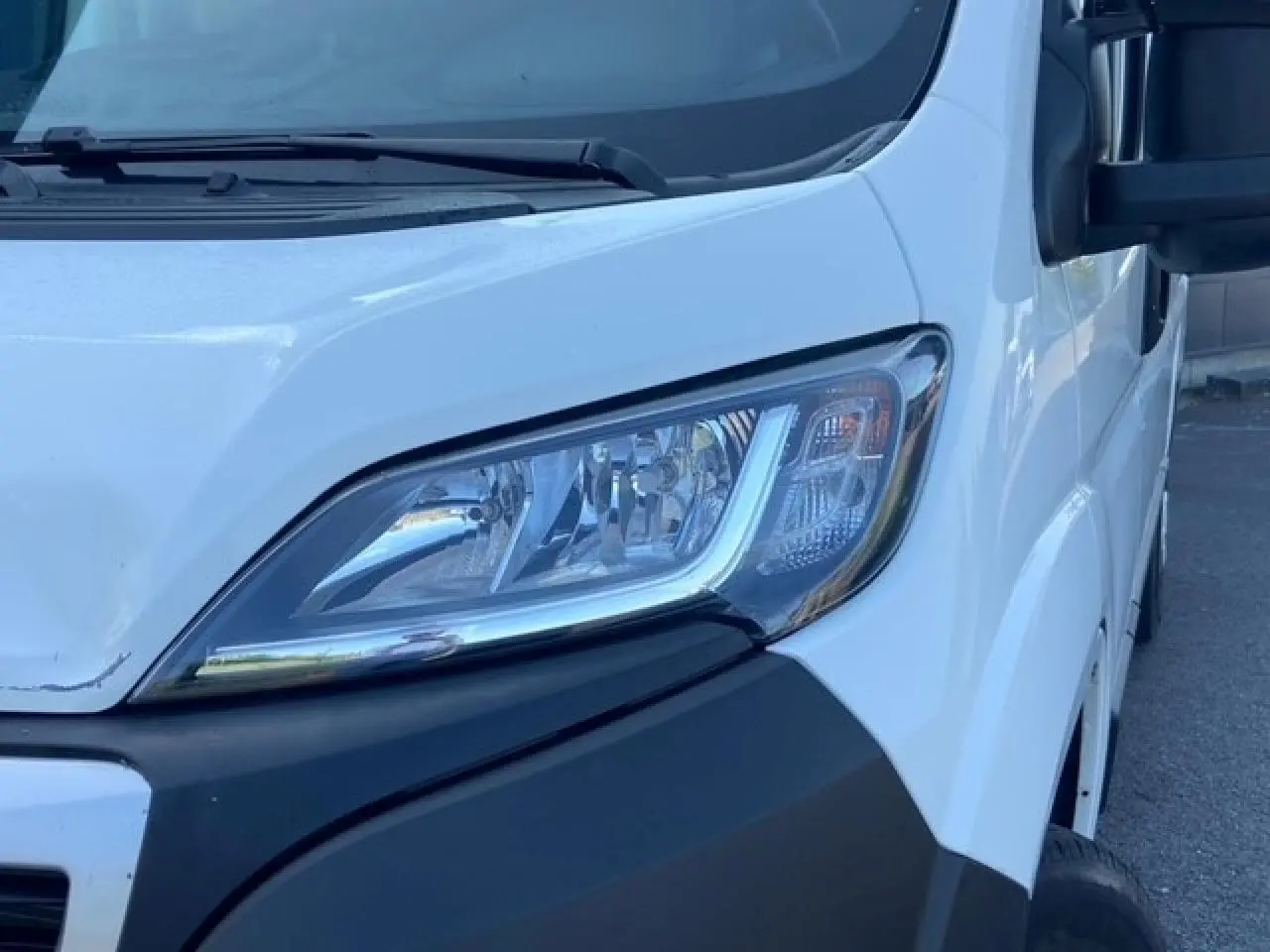 Gros plan sur le phare avant droit du Peugeot Boxer Fourgon blanc, soulignant la calandre et le rétroviseur noir.