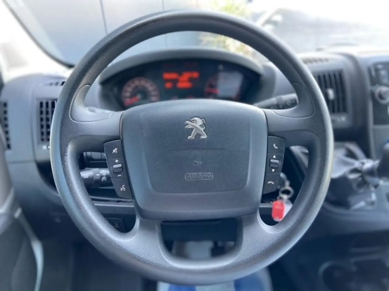 Vue rapprochée du volant Peugeot Boxer Fourgon 2019 avec commandes intégrées et tableau de bord flou en arrière-plan.
