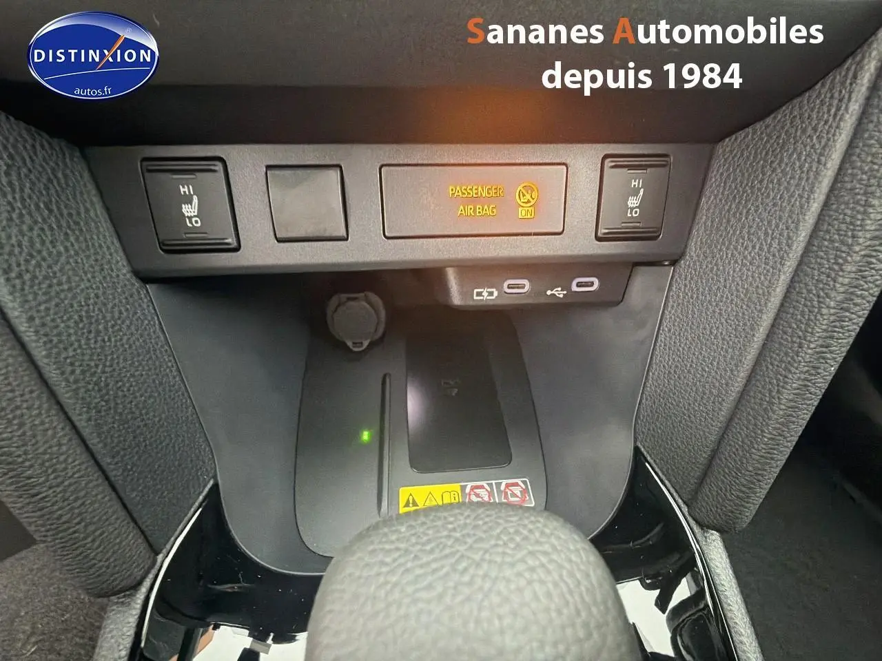 Gros plan sur la console centrale avec commandes sièges chauffants et ports USB d'une Toyota Yaris Cross blanche hybride 2025.