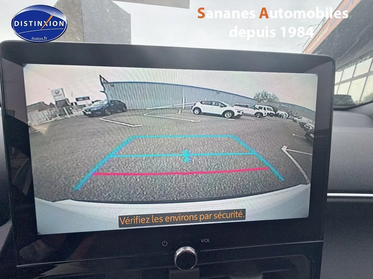 Écran tactile montrant la caméra de recul d'une Toyota Yaris Cross blanche, vue arrière avec lignes de guidage colorées.