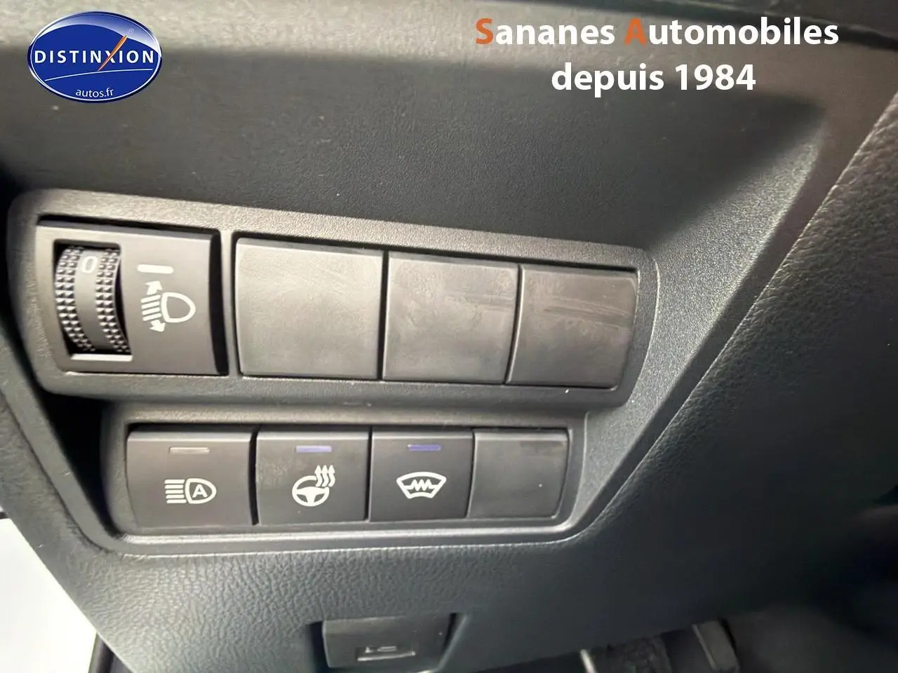 Gros plan sur les commandes de réglage d’éclairage et de chauffage du volant dans une Toyota Yaris Cross blanche, vue intérieure côté conducteur.