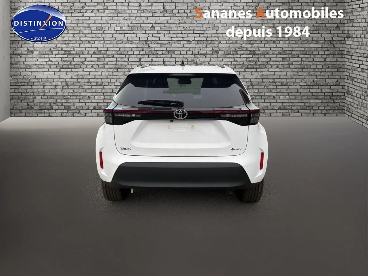 Vue arrière d'une Toyota Yaris Cross Hybrid 130h blanche, avec feux arrière reliés par une bande noire et pare-chocs noir.