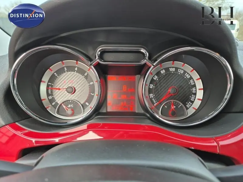 Gros plan sur le tableau de bord de l'Opel Adam Rocks, avec compte-tours et compteur de vitesse cerclés de chrome, sur fond rouge brillant.