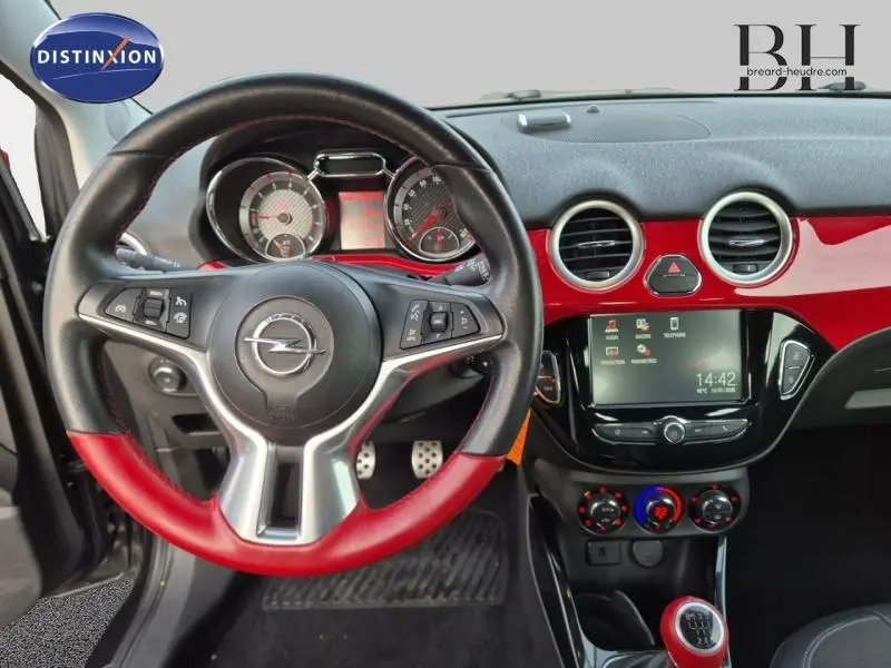 Vue intérieure centrée sur le volant cuir noir et rouge de l'Opel Adam Rocks avec tableau de bord rouge brillant et écran tactile.
