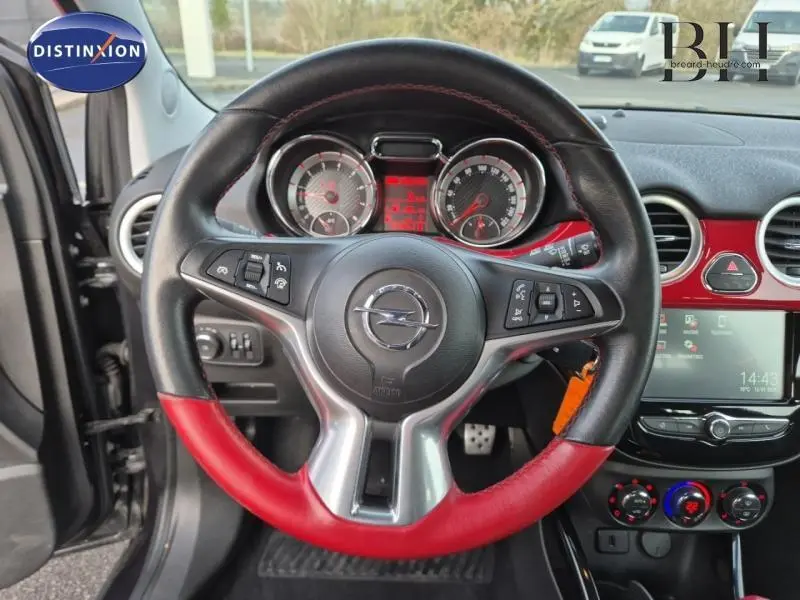 Vue intérieure centrée sur le volant cuir noir et rouge de l'Opel Adam Rocks avec tableau de bord et écran tactile visibles.