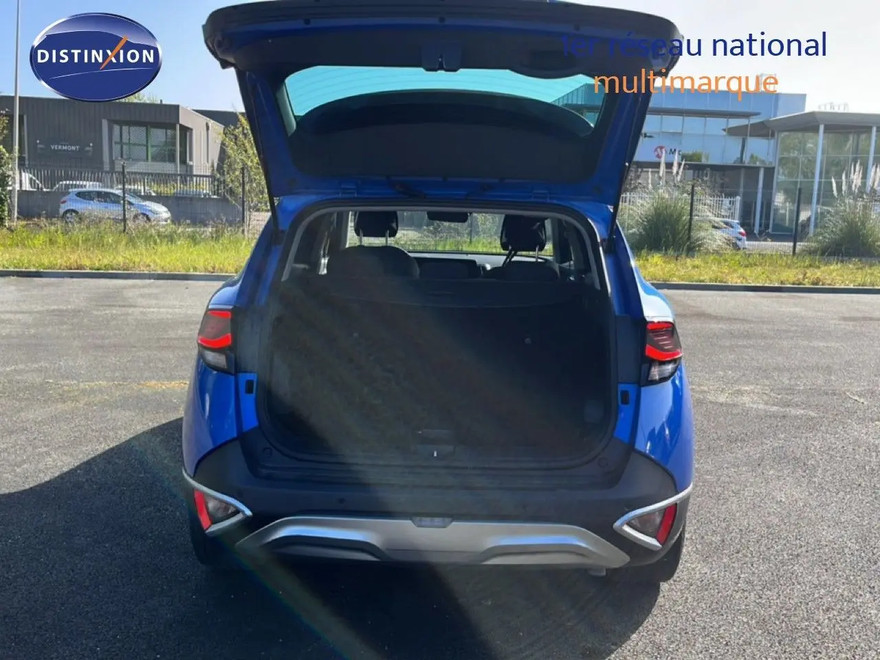 Vue arrière d'un KIA Sportage bleu fusion métal 2022 avec coffre ouvert, montrant l'espace de chargement et les feux arrière allumés.