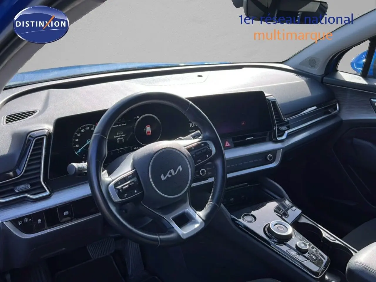 Vue intérieure du poste de conduite du Kia Sportage bleu fusion métal 2022, volant cuir multifonction et tableau de bord digital.
