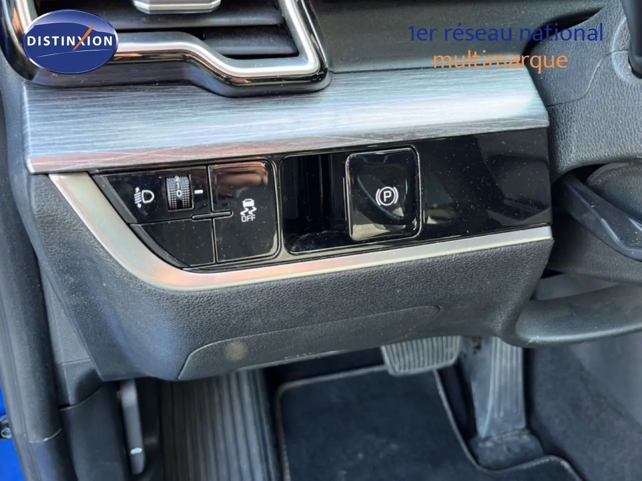Gros plan sur les commandes sous le tableau de bord côté gauche du Kia Sportage bleu fusion métal 2022, avec bouton de frein à main électrique.