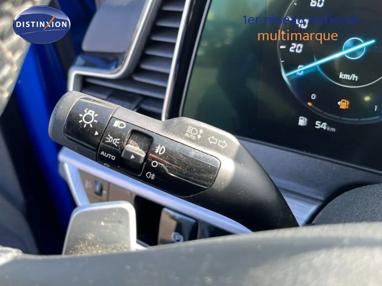 Gros plan sur la manette de clignotants et phares du KIA Sportage bleu fusion, avec tableau de bord numérique en arrière-plan.