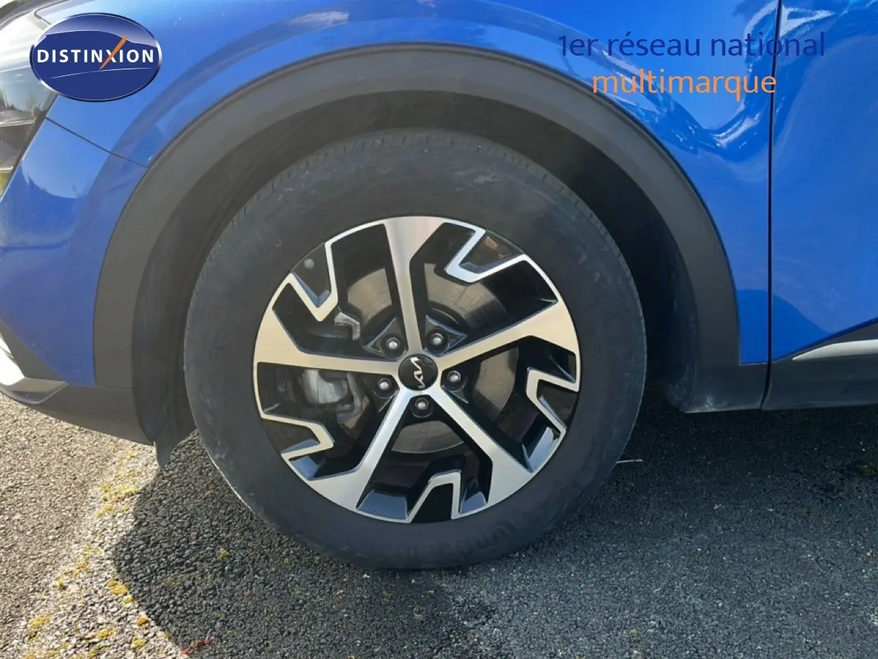 Gros plan sur la roue avant gauche du Kia Sportage bleu fusion métal, mettant en valeur la jante alliage au design moderne.