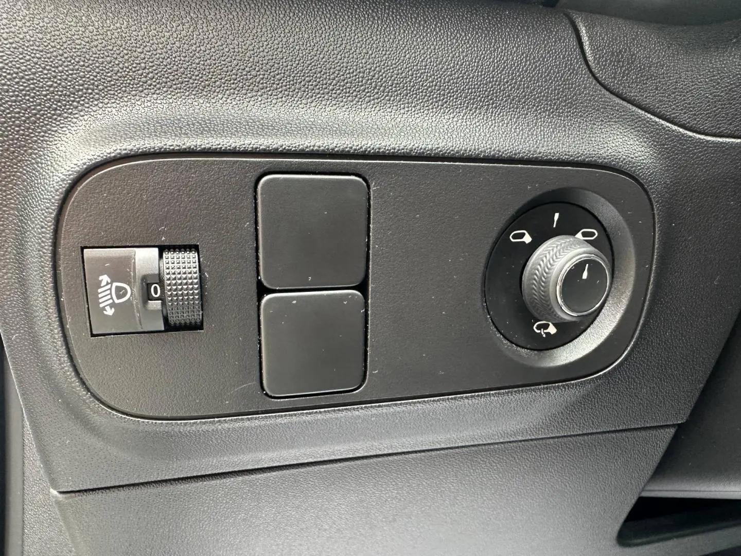 Gros plan sur les commandes noires de réglage des rétroviseurs et des phares d’un Citroën C3 blanc Banquise 2023.