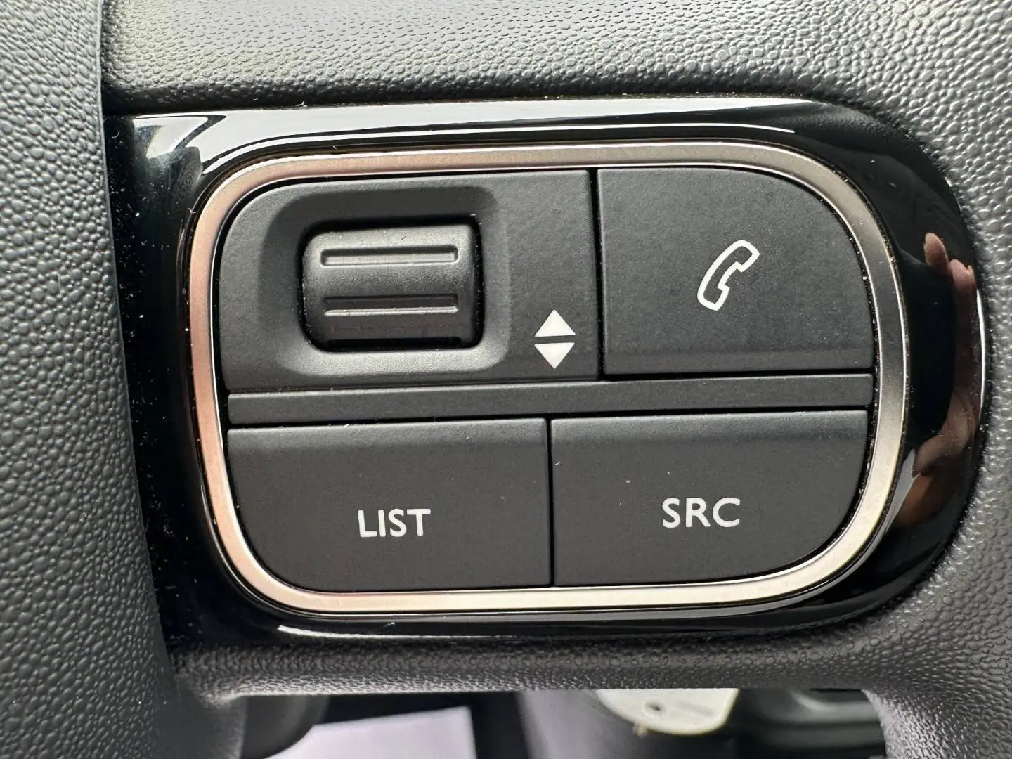 Gros plan sur les commandes noires du volant de la Citroën C3 2023, boutons pour téléphone et audio.