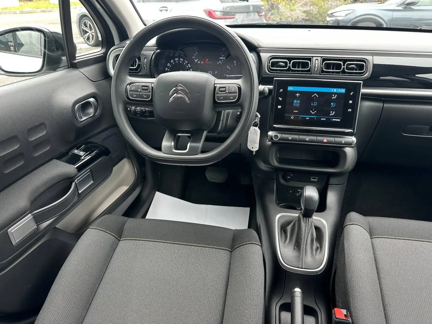 Vue intérieure avant de la Citroën C3 blanche, montrant le volant, l'écran tactile et la console centrale avec levier de vitesse automatique.