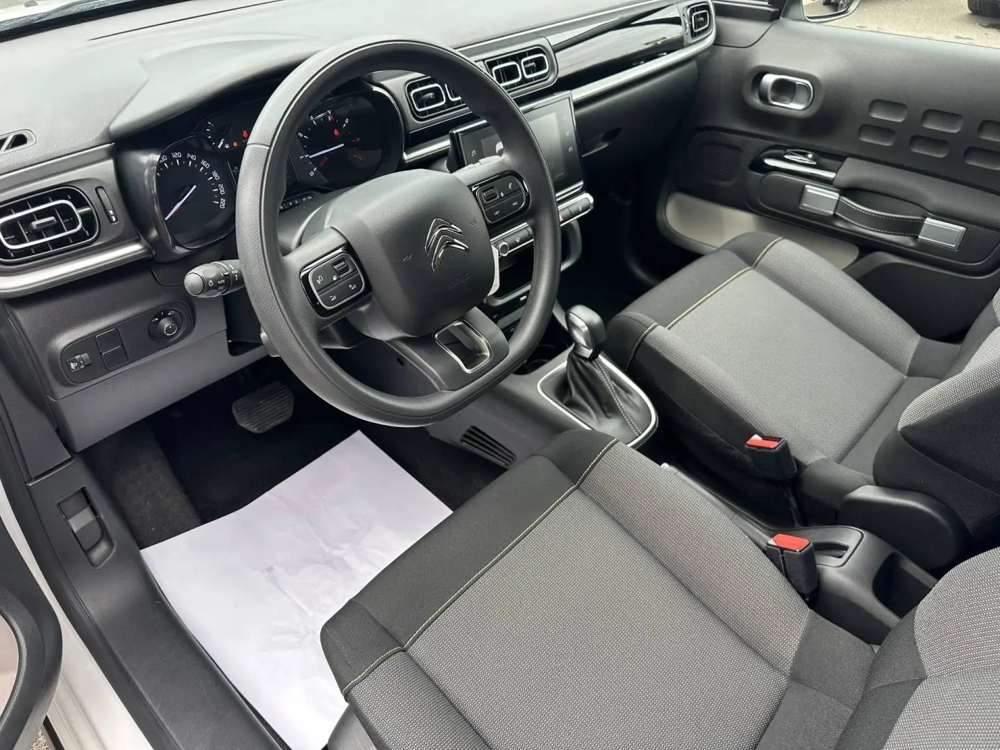 Vue intérieure côté conducteur de la Citroën C3 2023, montrant le volant, la console centrale avec écran tactile et sièges gris tissu Mica Grey.