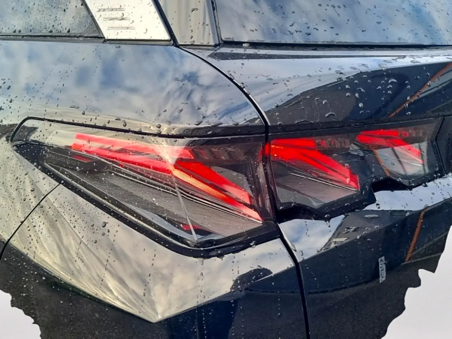 Gros plan sur le feu arrière droit rouge du Peugeot 5008 noir avec gouttes de pluie sur la carrosserie.