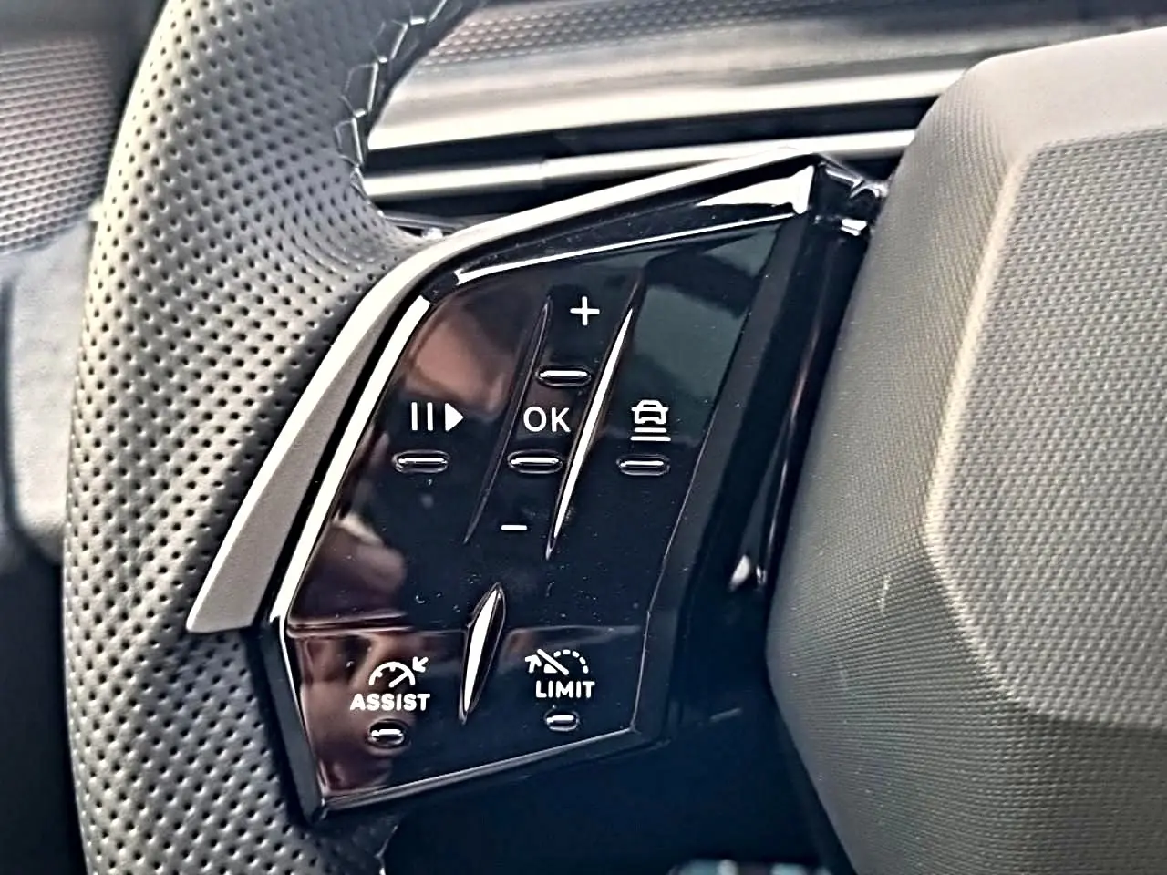 Gros plan sur les commandes noires du volant cuir perforé du Peugeot 5008 Hybrid 145 GT e-DCS6, côté gauche.