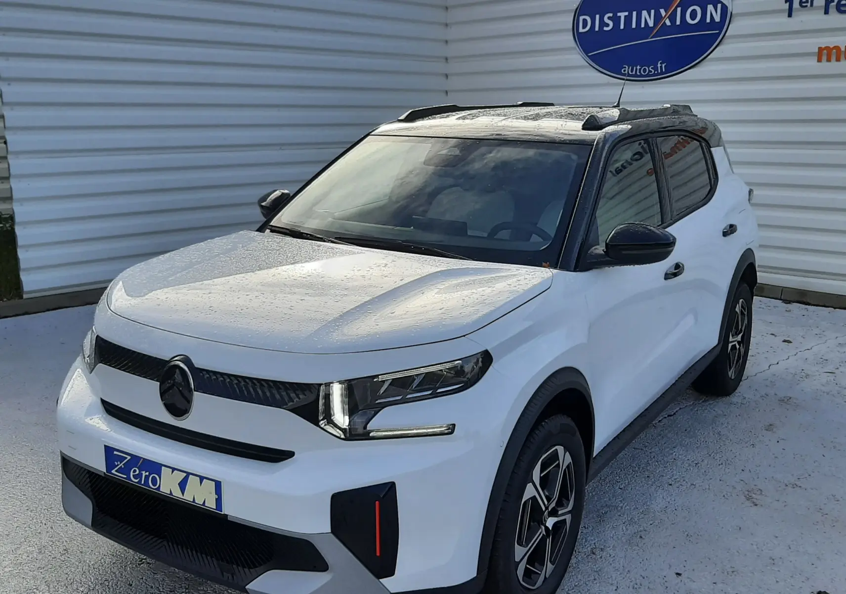 Vue 3/4 avant droite d'une Citroën C3 Aircross blanche avec toit noir, feux LED et jantes bi-ton, stationnée devant un mur blanc.