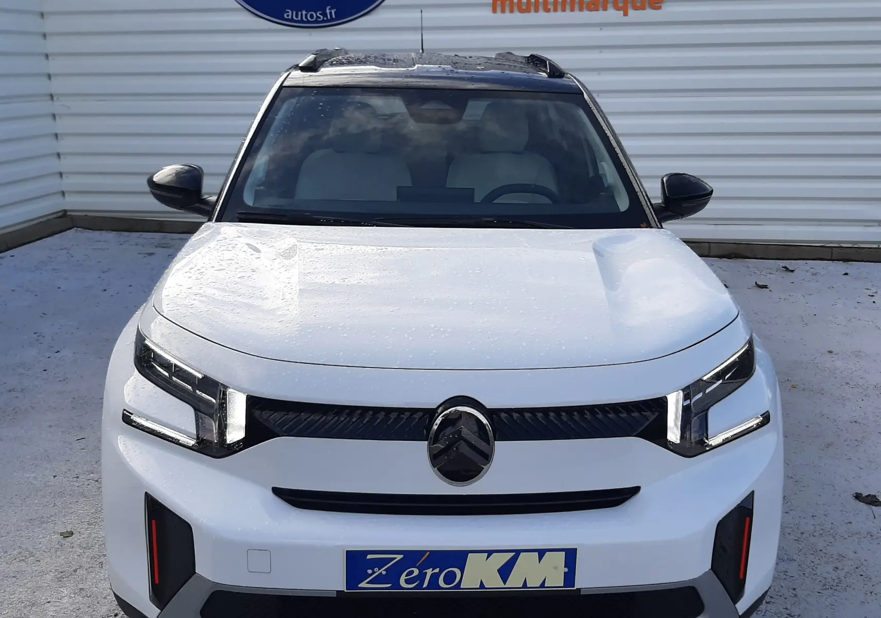 Vue avant d'une Citroën C3 Aircross 2026 blanc avec toit noir, feux LED et plaque Zéro KM visible.