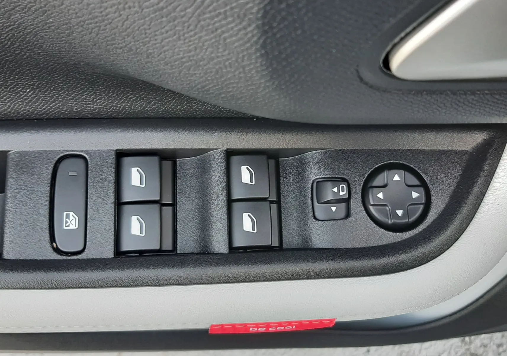 Gros plan sur les commandes de lève-vitres et réglage des rétroviseurs côté conducteur d'une Citroën C3 Aircross blanc toit noir.