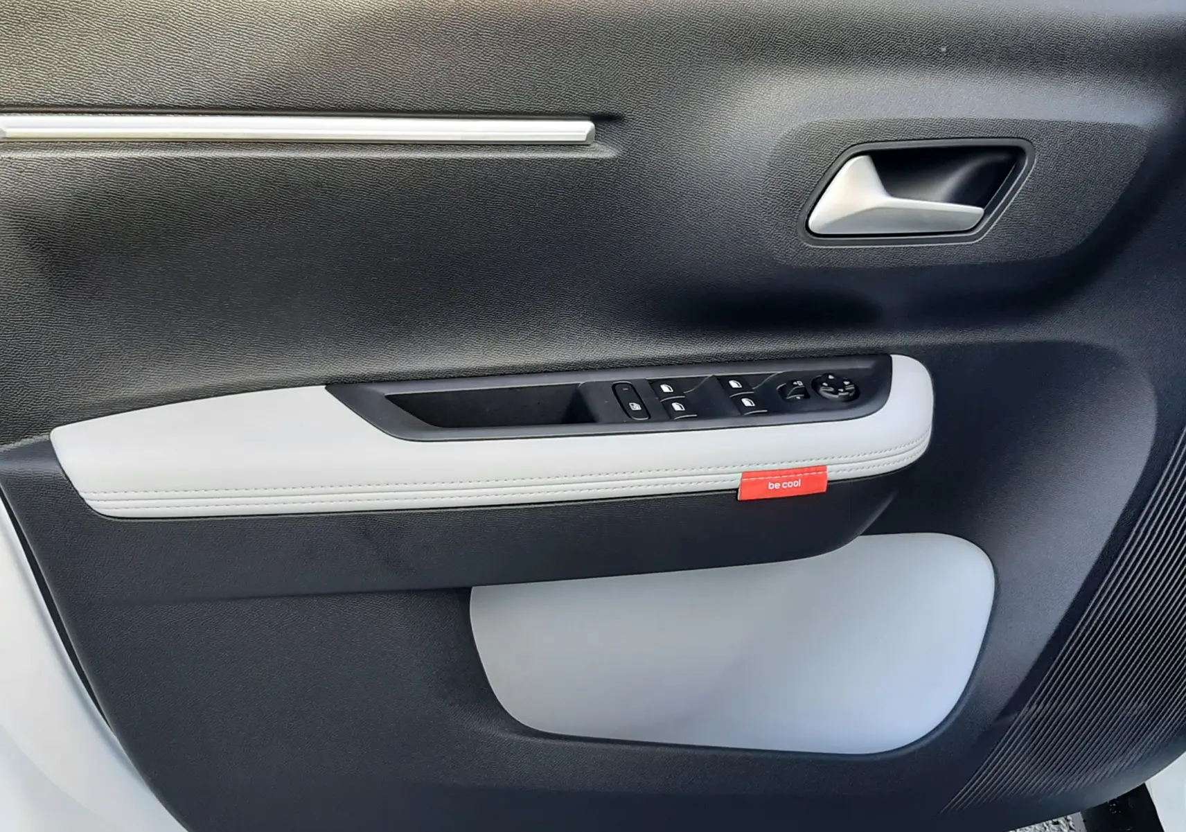 Vue rapprochée de la porte avant gauche du Citroën C3 Aircross 2026 blanc/toit noir, avec garniture bicolore et bouton "be cool".