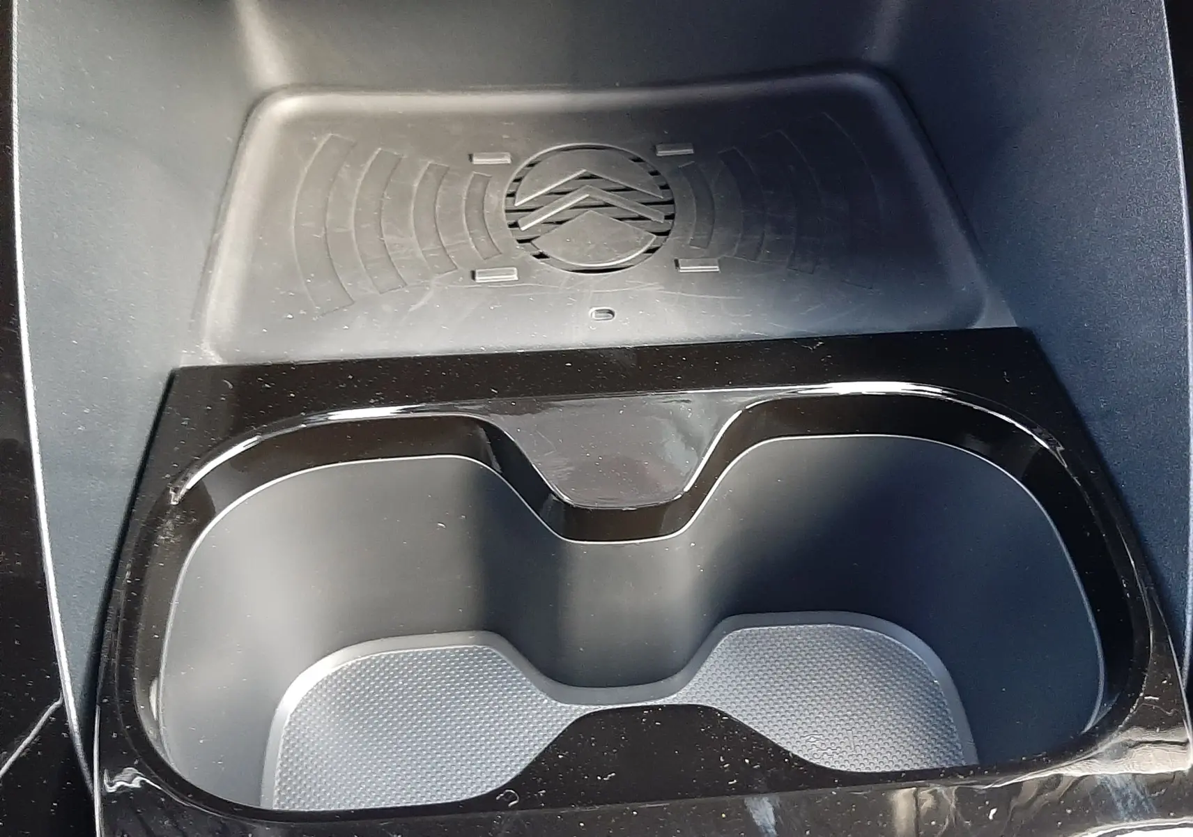 Gros plan intérieur sur le compartiment porte-gobelets noir brillant avec zone de charge sans fil et logo Citroën embossé.