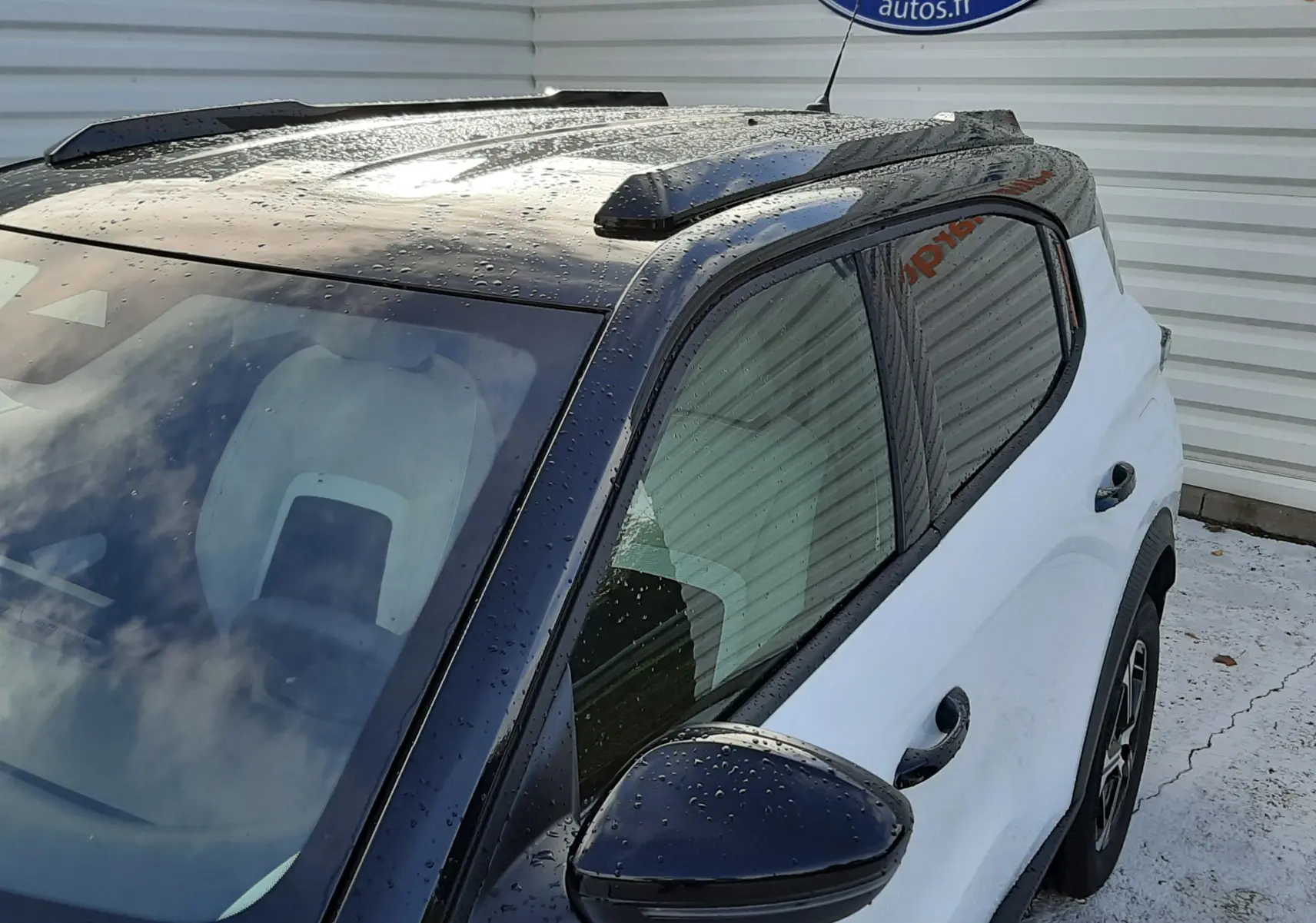 Vue 3/4 avant droit du Citroën C3 Aircross blanc avec toit noir brillant et rétroviseur noir sous la pluie.