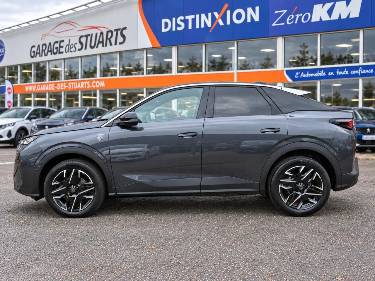 Vue latérale droite d'un Peugeot 3008 gris titane avec jantes alliage 19 pouces diamantées, garé devant un garage.