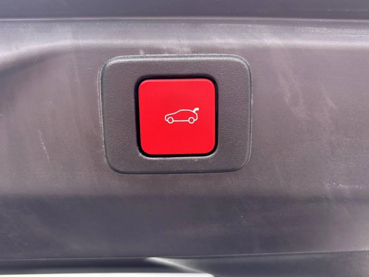 Bouton rouge d'ouverture électrique du hayon sur le coffre d'un Peugeot 3008 gris titane.