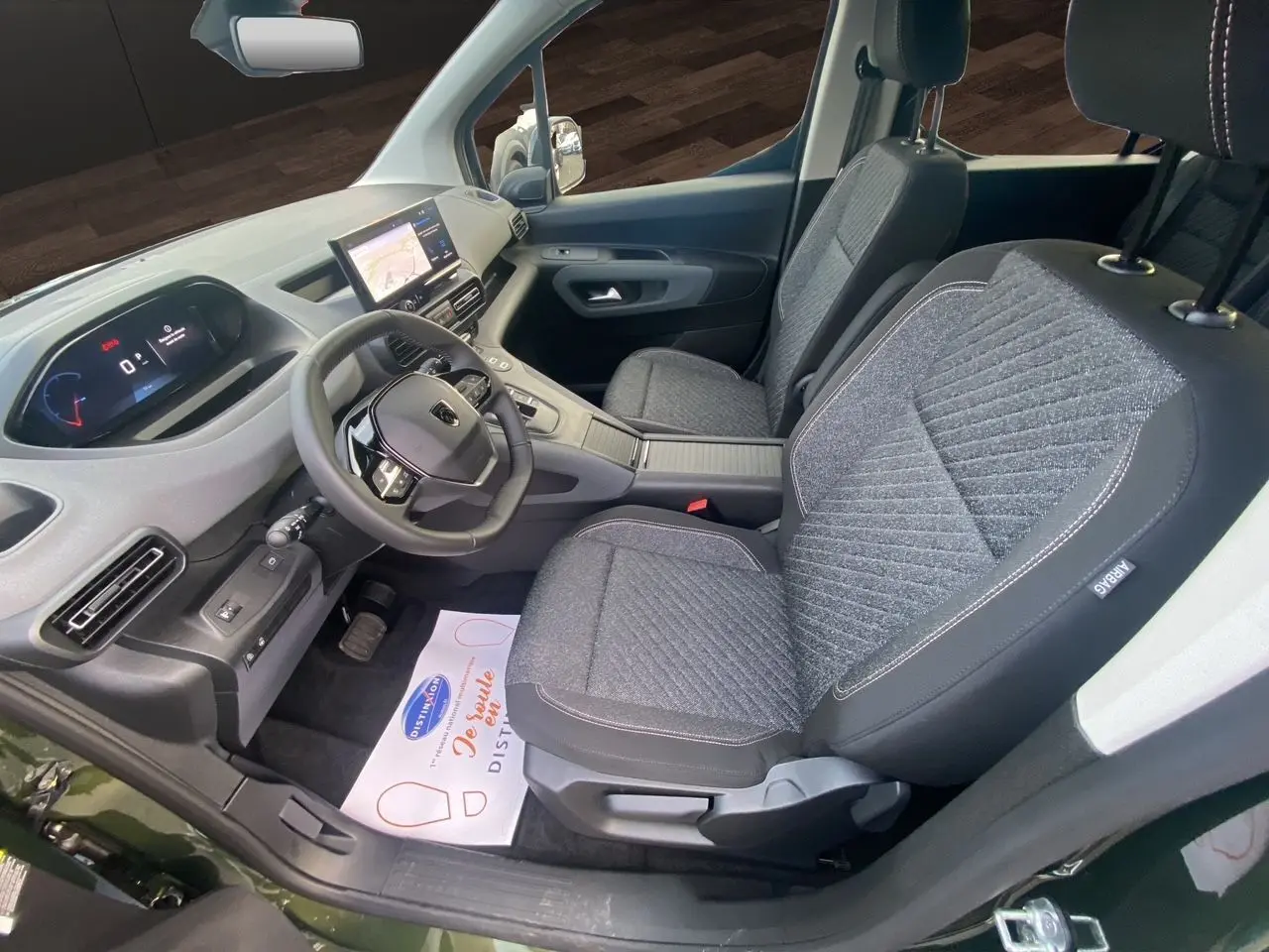 Vue intérieure côté conducteur du Peugeot Rifter 2025, sièges gris tissu et tableau de bord moderne avec écran tactile.