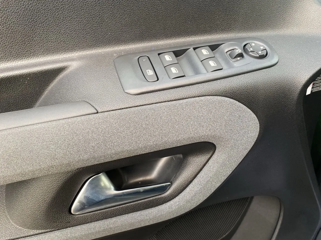 Gros plan sur la poignée intérieure et les commandes des vitres côté conducteur du Peugeot Rifter 2025, finition tissu gris-noir.
