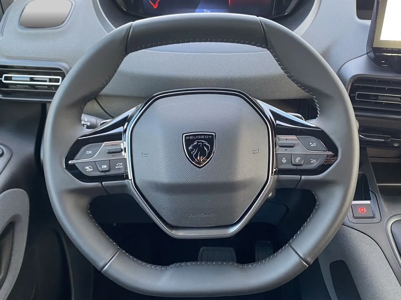 Vue rapprochée du volant cuir noir avec logo Peugeot du Rifter 2025, mettant en valeur les commandes multifonctions.