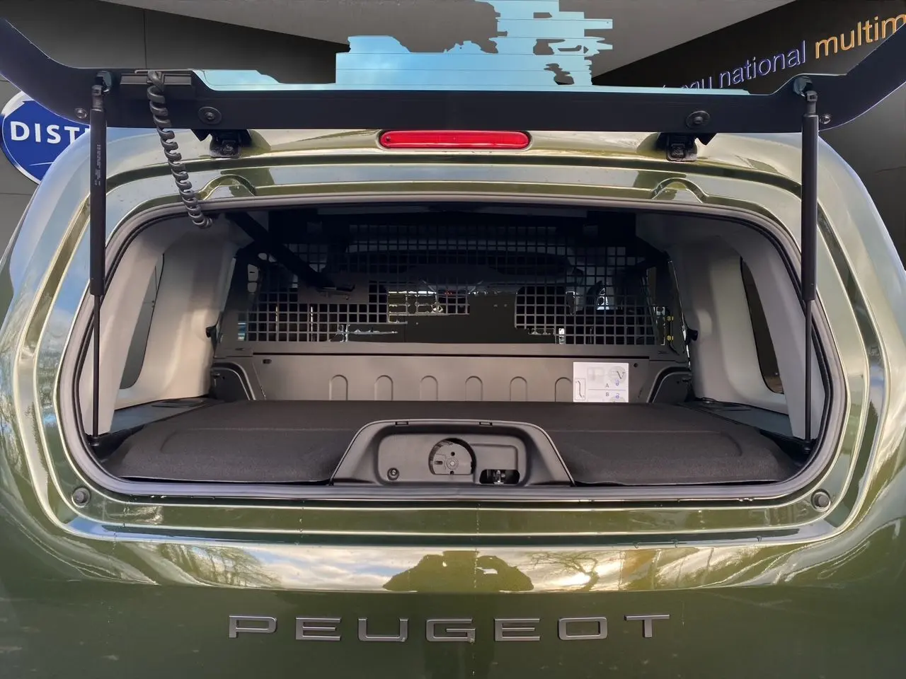 Vue arrière du Peugeot Rifter 2025 vert Sirkka Green avec hayon ouvert et cloison de séparation visible dans le coffre.