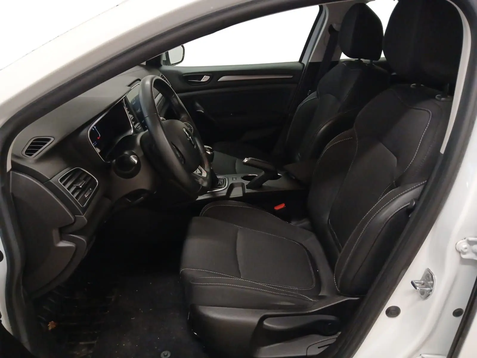 Vue intérieure côté conducteur de la Renault Mégane IV blanche, montrant les sièges noirs et le tableau de bord.
