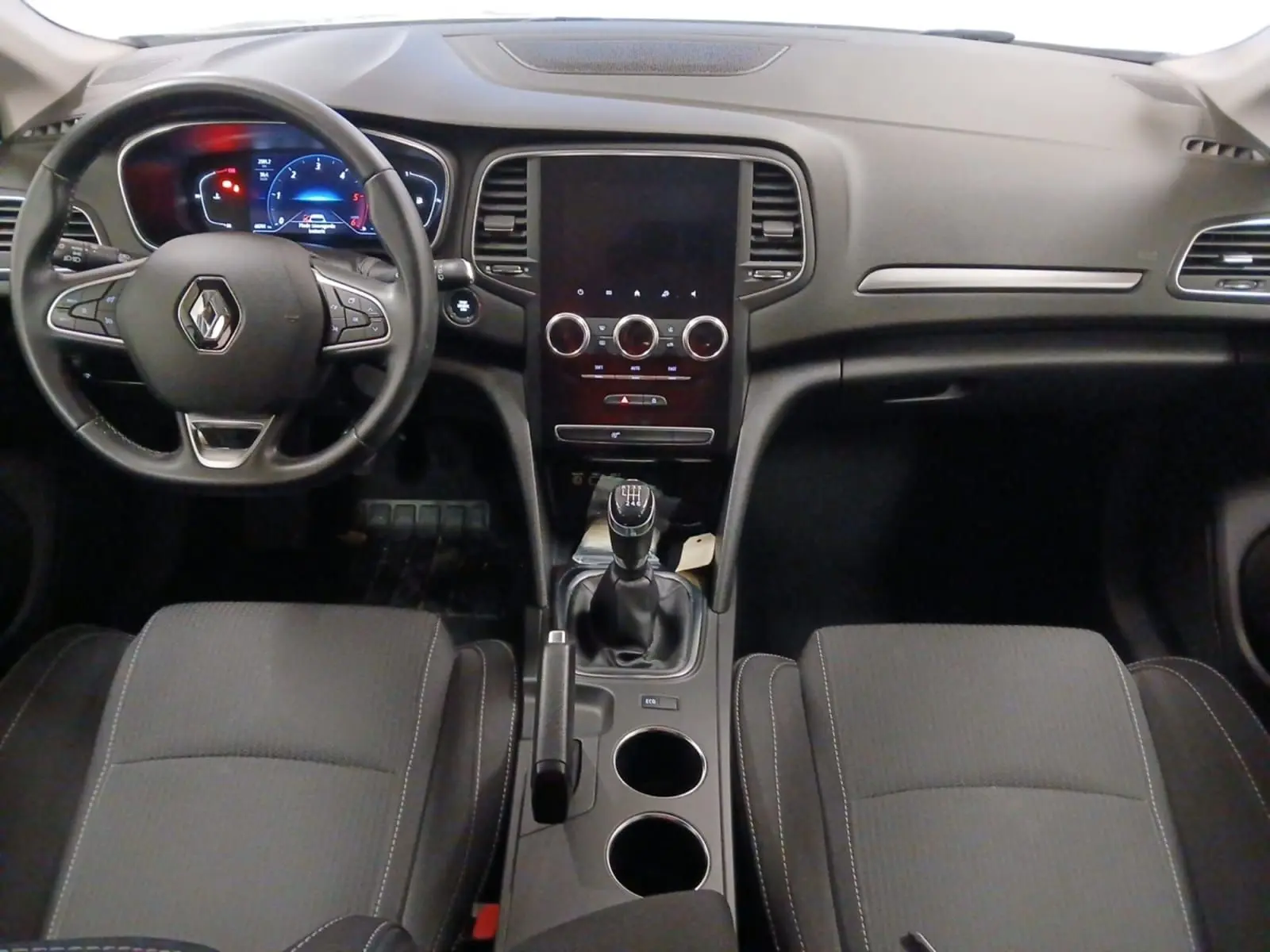 Vue intérieure frontale de la Renault Mégane IV 2020 avec tableau de bord noir, volant multifonction et boîte manuelle.