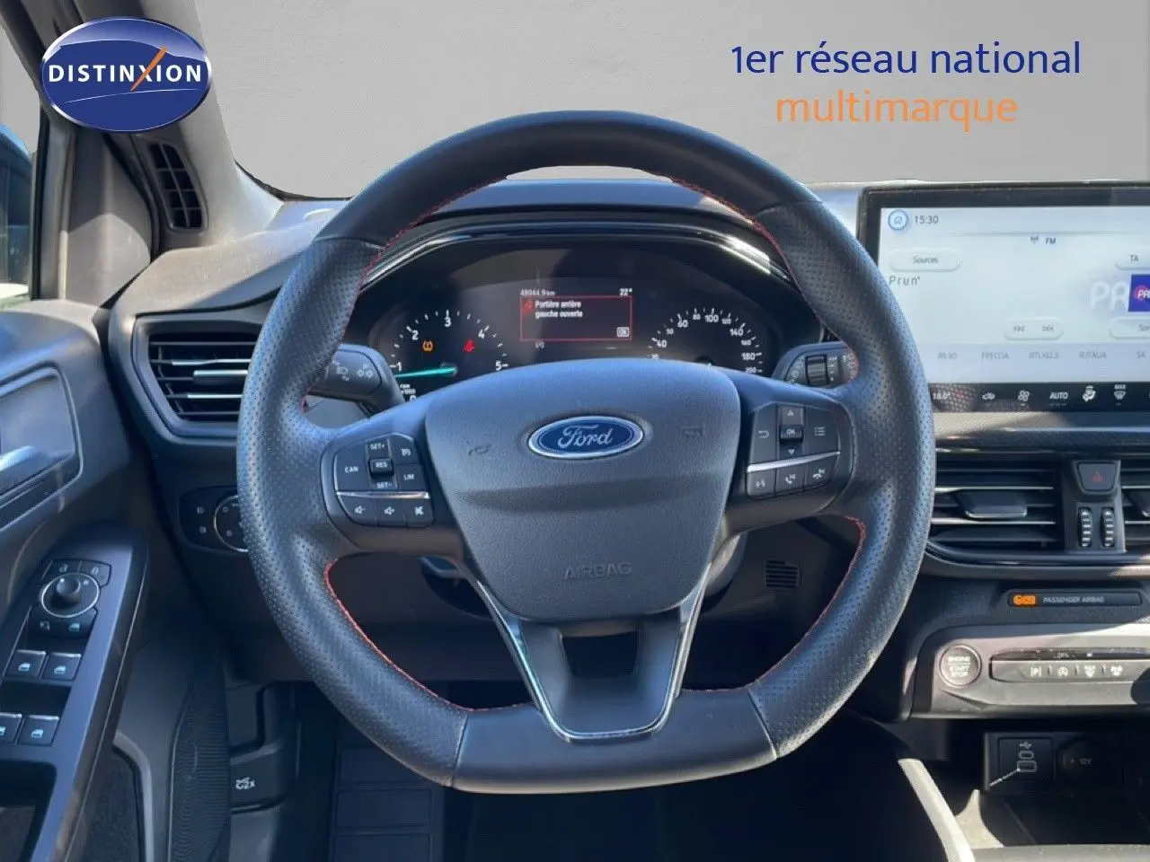 Vue centrée sur le volant en cuir perforé de la Ford Focus SW 2024 noir agate, avec tableau de bord et écran tactile visibles.