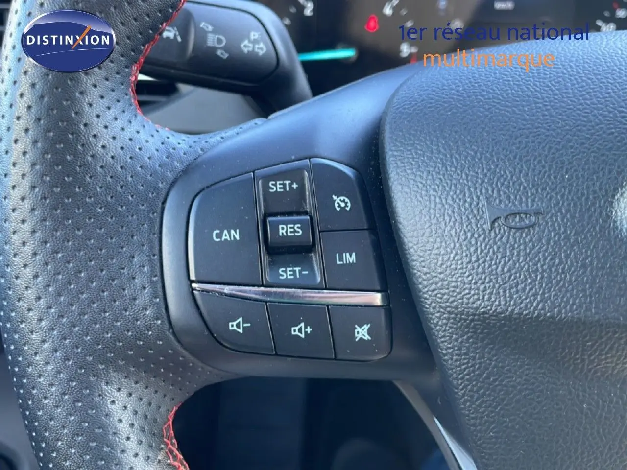Gros plan sur le volant noir perforé avec surpiqûres rouges de la Ford Focus SW 2024, boutons de régulateur de vitesse visibles.