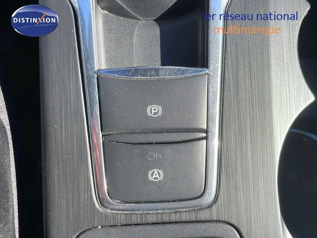 Gros plan sur la console centrale de la Ford Focus SW noire, mettant en valeur les boutons du frein à main électrique et de l'assistance au démarrage.
