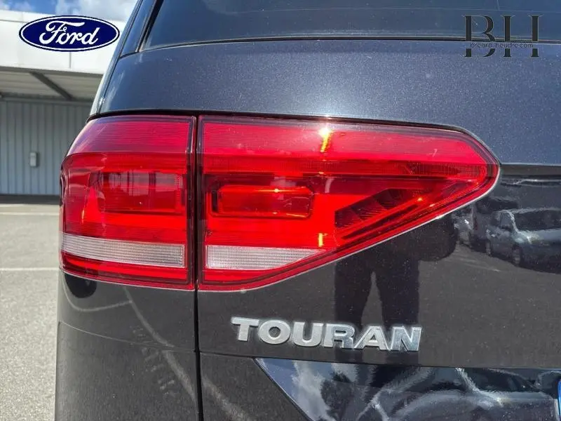 Gros plan sur le feu arrière gauche d’un Volkswagen Touran noir intense nacré avec logo et nom du modèle visibles.