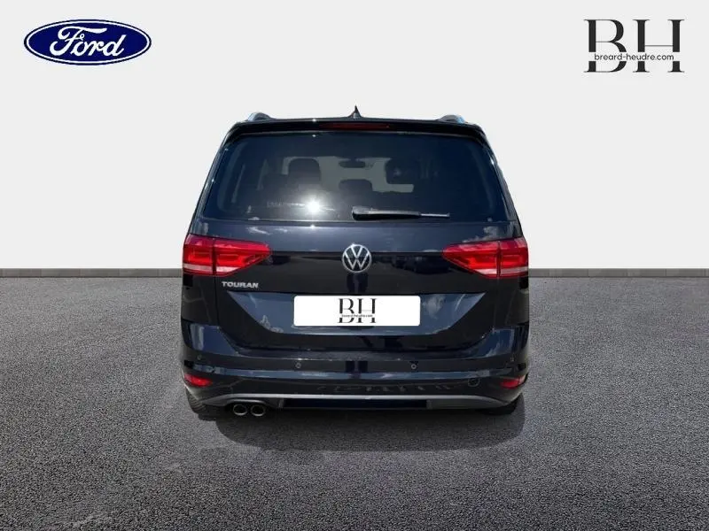 Vue arrière d'un Volkswagen Touran noir intense nacré, avec feux rouges et double sortie d'échappement visible côté gauche.