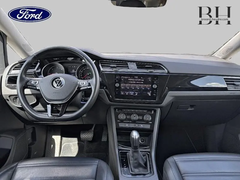 Vue intérieure avant du Volkswagen Touran 2.0 TDI 2020 avec volant cuir multifonction et console centrale noire brillante.