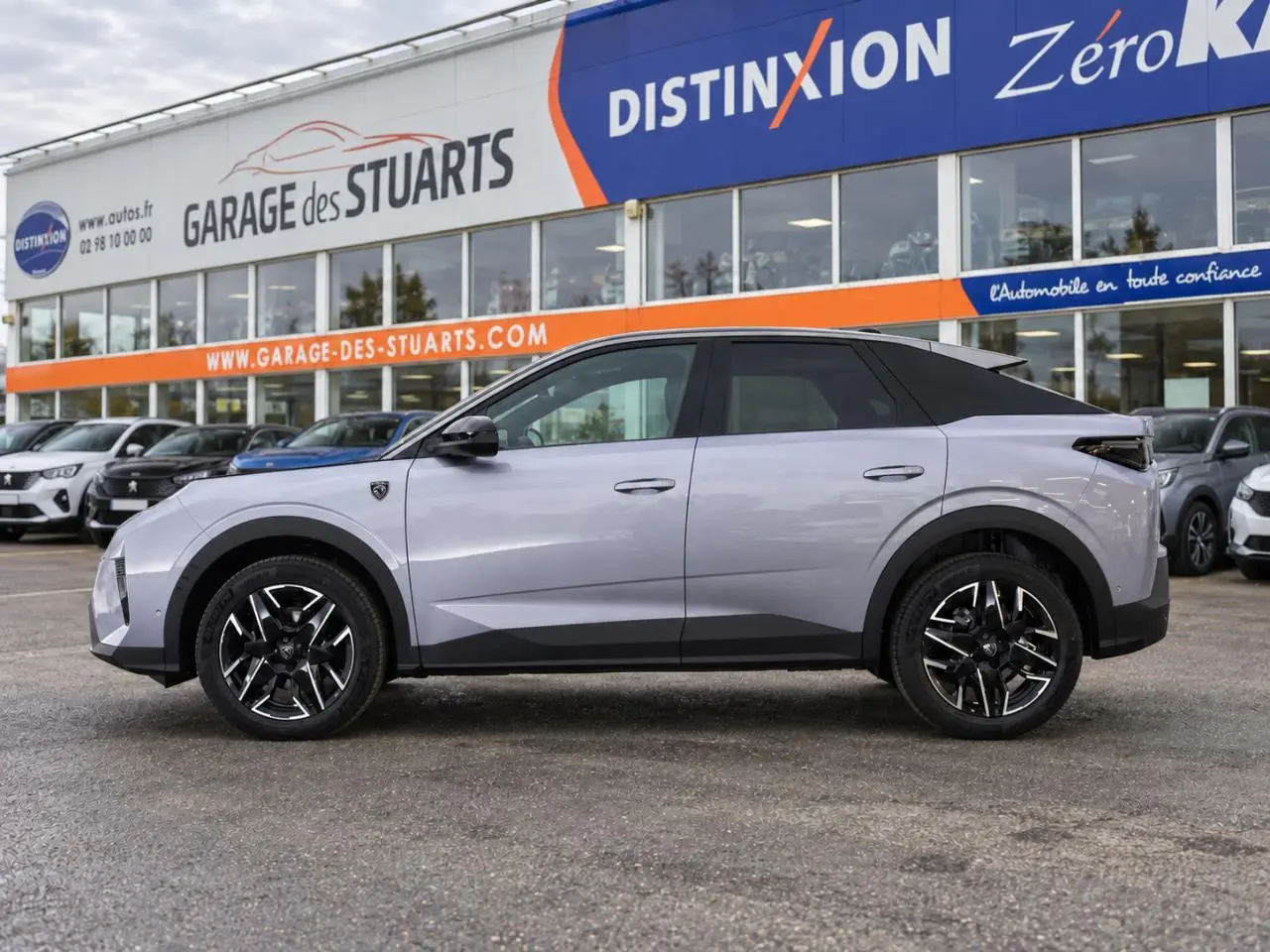 Vue de profil côté gauche du Peugeot 3008 gris Artense avec jantes alliage noires et toit noir, devant un garage.