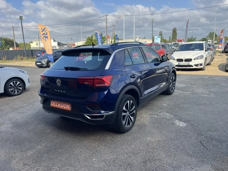 Vue 3/4 arrière droite d'un Volkswagen T-Roc bleu foncé avec jantes alliage, sur un parking extérieur.