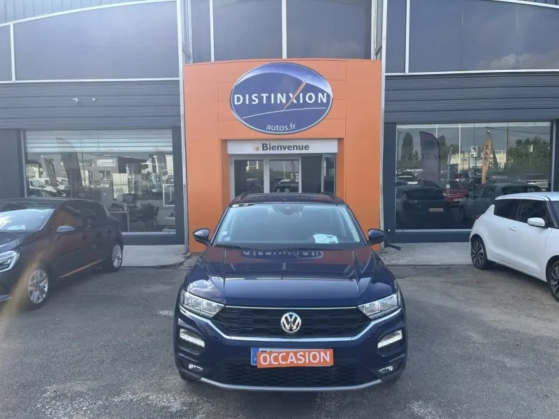 Volkswagen T-Roc bleu foncé vue de face, stationné devant un garage avec panneau orange "Distinxion".