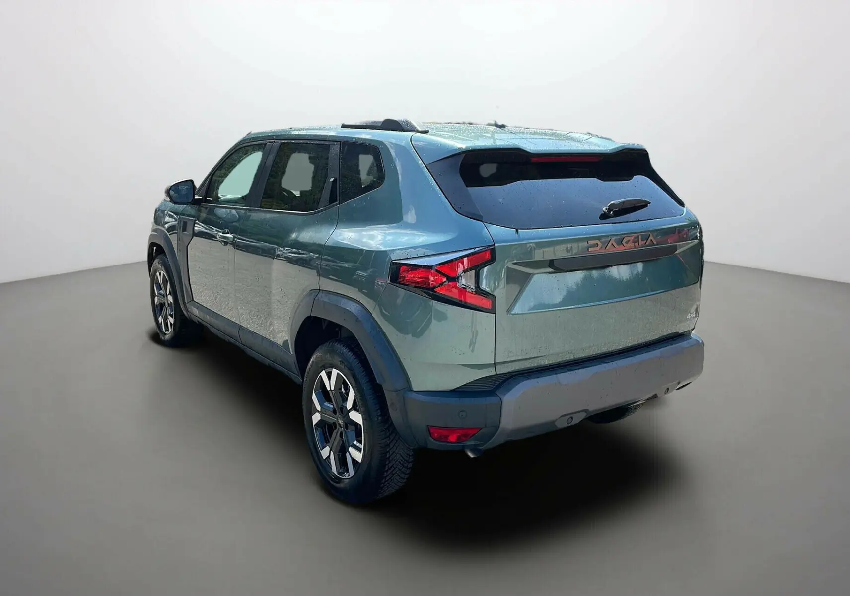Vue 3/4 arrière droite du Dacia Duster 2025 vert cèdre avec jantes alliage et logo DACIA en relief sur le hayon.