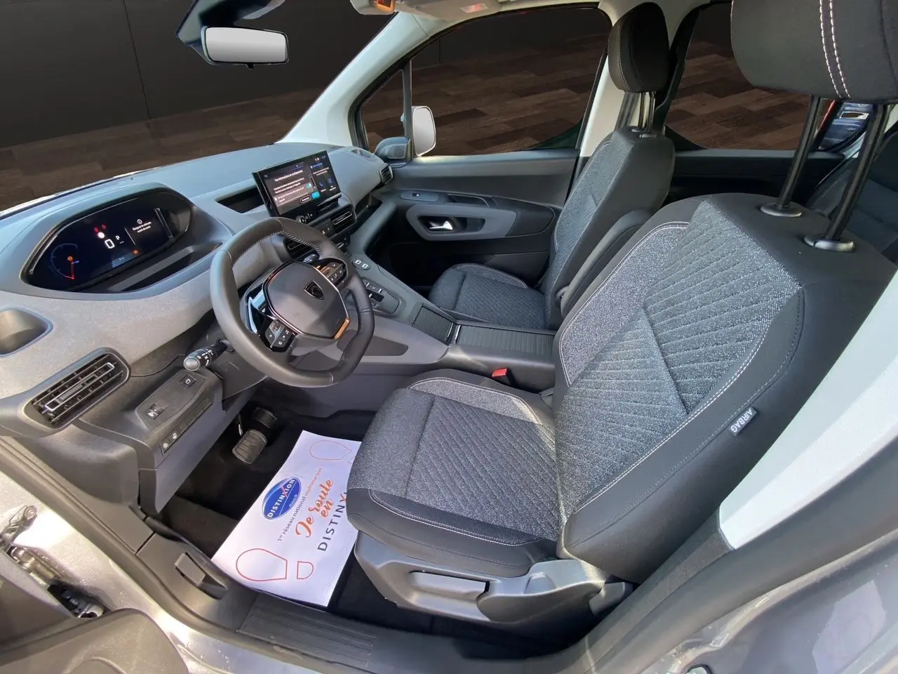 Vue intérieure côté conducteur du Peugeot Rifter 2025 gris acier, avec tableau de bord numérique et sièges tissu gris.