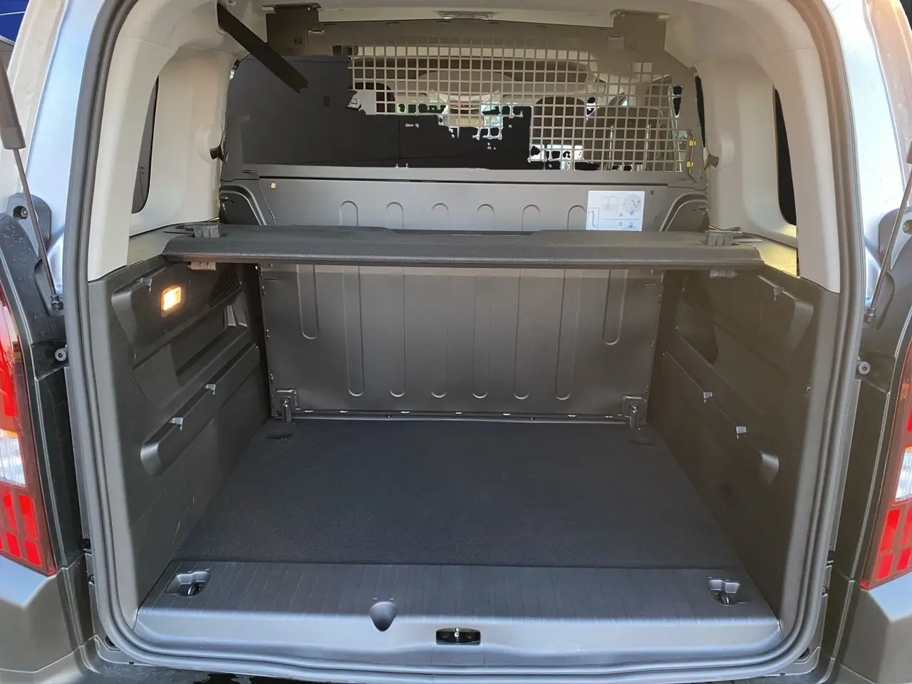 Coffre ouvert vu de l'arrière du Peugeot Rifter gris acier avec cloison métallique et tablette de séparation.