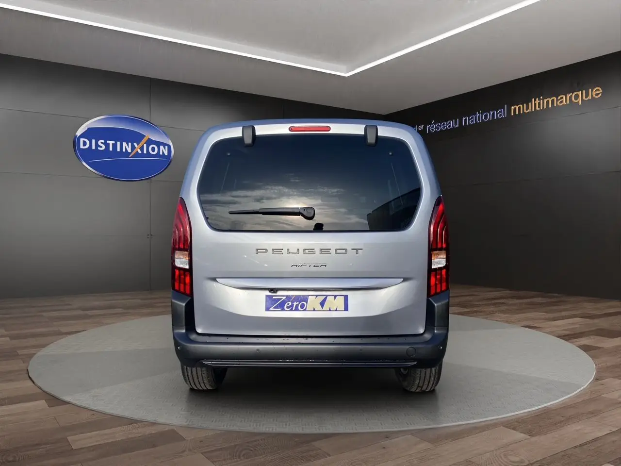 Vue arrière du Peugeot Rifter gris acier 2025 avec hayon vitré et feux arrière verticaux allumés.