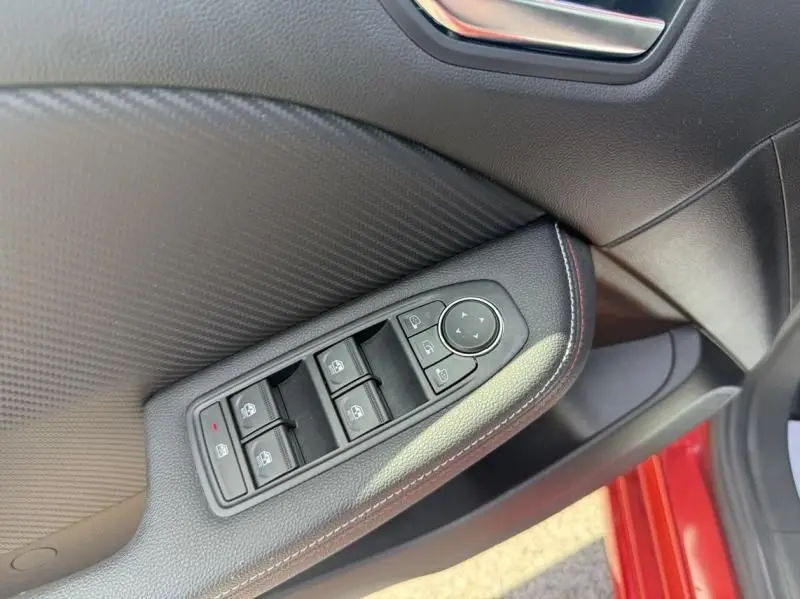 Gros plan sur la commande des vitres électriques côté conducteur de la Renault Clio V Rouge Flamme, avec surpiqûres rouges.