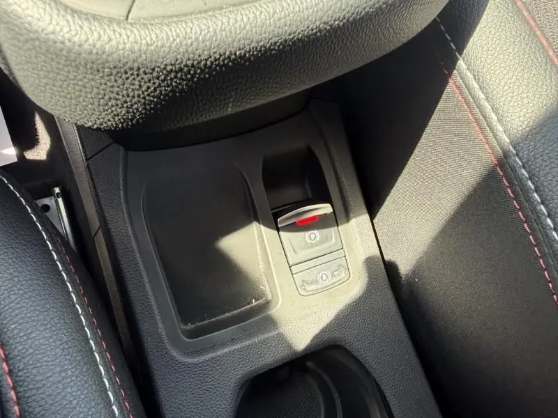 Gros plan sur la console centrale de la Renault Clio V Rouge Flamme, mettant en valeur le frein à main électronique et les surpiqûres rouges.