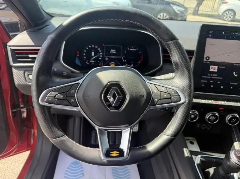 Vue centrée sur le volant de la Renault Clio V Rouge Flamme 2022, avec tableau de bord digital et écran tactile visible.